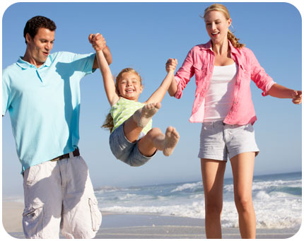A young couple swing their child between them at the beach